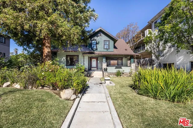 a view of a house with a small yard plants and large trees