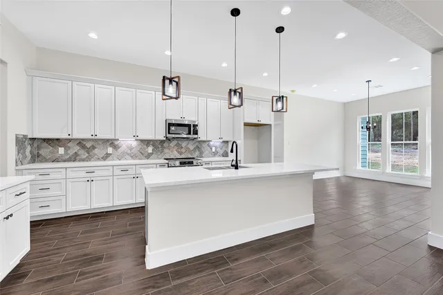 a kitchen with stainless steel appliances granite countertop a sink a window and white cabinets