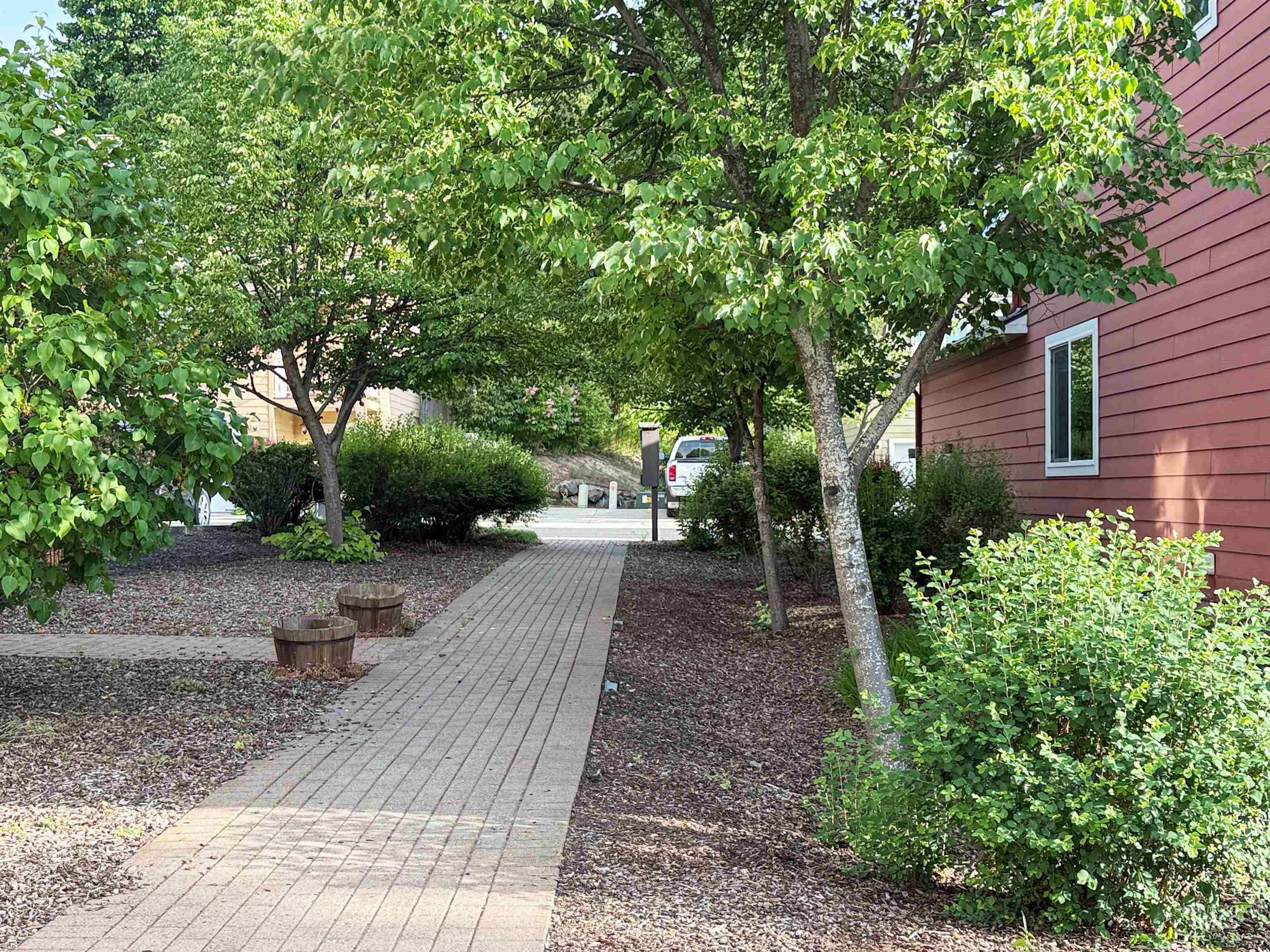 1354 Bristol Road Moscow, ID 83843 - Photo 15 of 19 Paver walkway bordered by mature trees and shrubs, with a red-sided building featuring a white-framed window