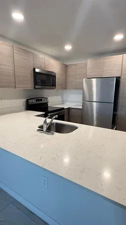 a kitchen with stainless steel appliances a sink a stove a microwave a sink a refrigerator and white cabinets