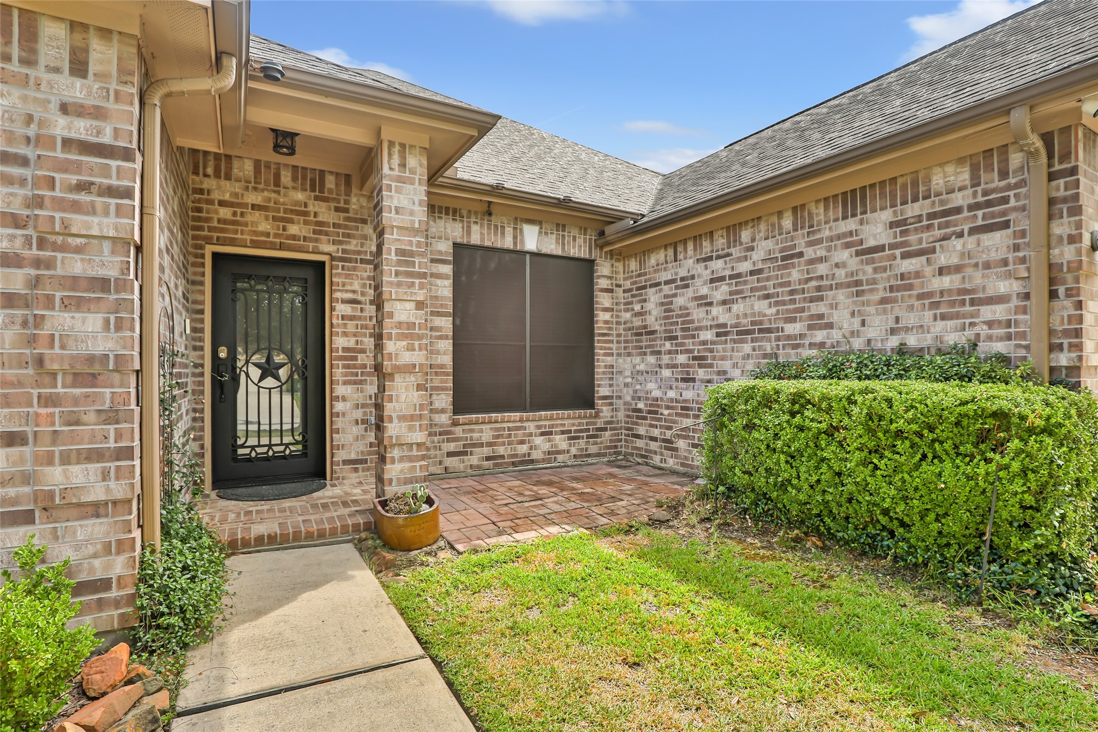 Charming entryway features a classic brick exterior, a welcoming wrought iron door, and a cozy patio space surrounded by lush greenery.