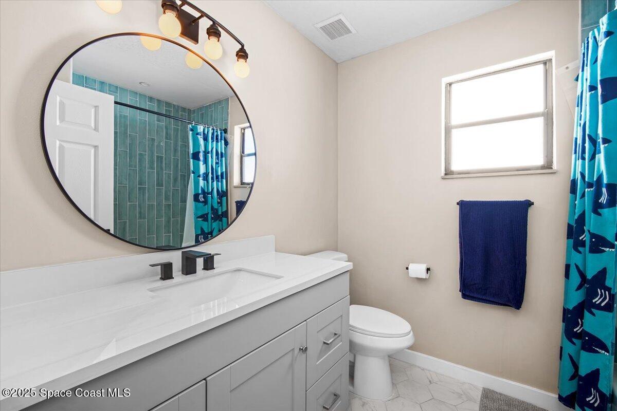 1709 Palm Ridge Road Melbourne, FL 32935 - Photo 21 of 43 a bathroom with a sink a mirror a toilet and a window