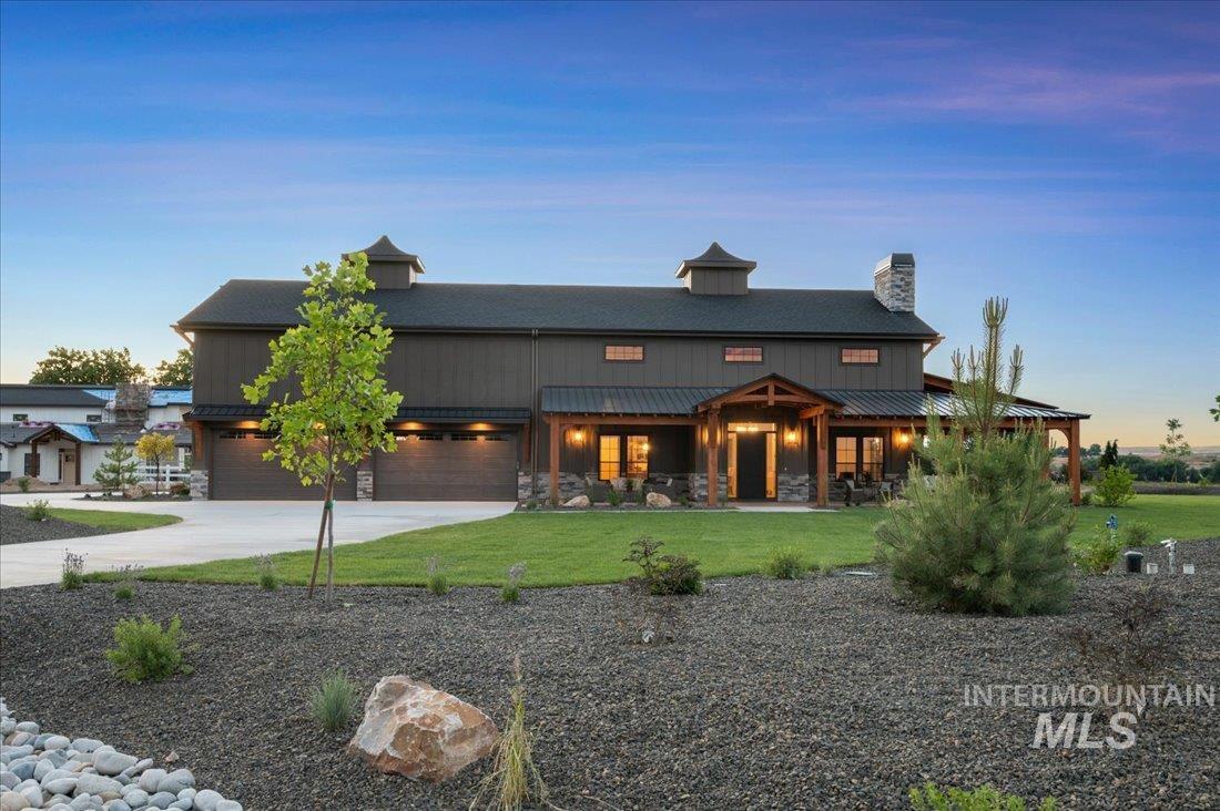 Rear view of house featuring stone siding, concrete driveway, a lawn, and a chimney