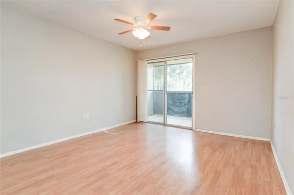a view of an empty room with wooden floor and a fan