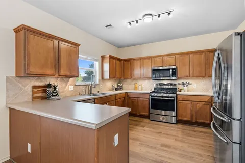 a kitchen with a refrigerator a stove top oven a sink dishwasher and wooden cabinets with wooden floor