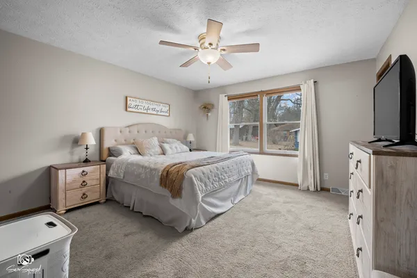 a spacious bedroom with a bed and a flat tv screen on the dresser