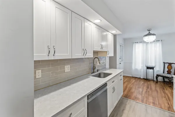 a kitchen with a sink dishwasher a stove and white cabinets with wooden floor