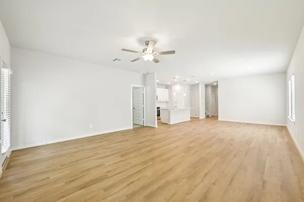 a view of an empty room with chandelier fan and wooden floor