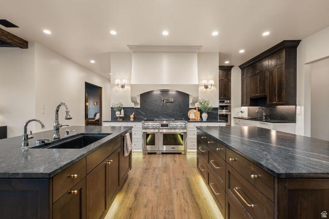 4871 South Homestead Way Washington, UT 84780 - Photo 26 of 151 Two tone kitchen featuring a large island with sink, decorative backsplash, stainless steel appliances, dark stone counters, and light wood-style flooring