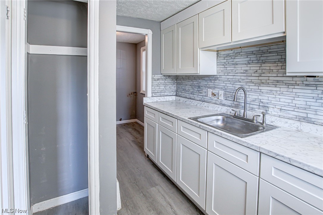 3423 Westbury Road Cleveland, OH 44120 - Photo 22 of 38 Kitchen featuring backsplash, a textured ceiling, white cabinets, light hardwood / wood-style floors, and sink
