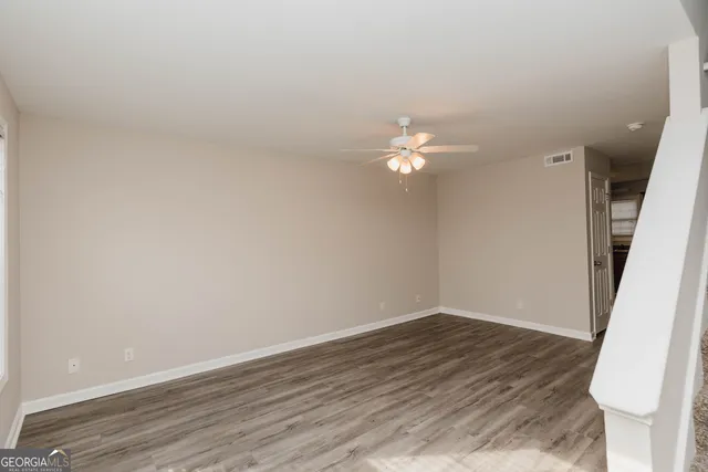 an empty room with wooden floor fan and windows