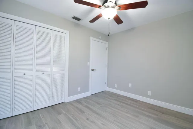 an empty room with wooden floor ceiling fan and windows