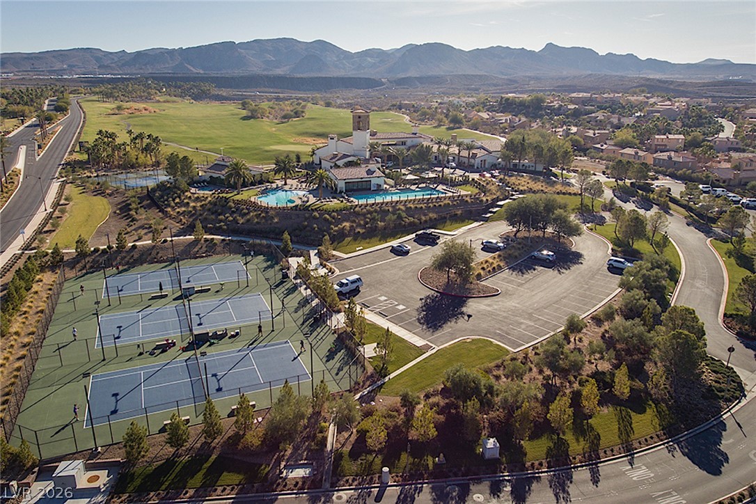 25 Falling Ridge Lane Henderson, NV 89011 - Photo 36 of 48 An aerial panorama reveals a vast community offering tennis courts, a shimmering pool, and a sprawling golf course against a mountain backdrop.