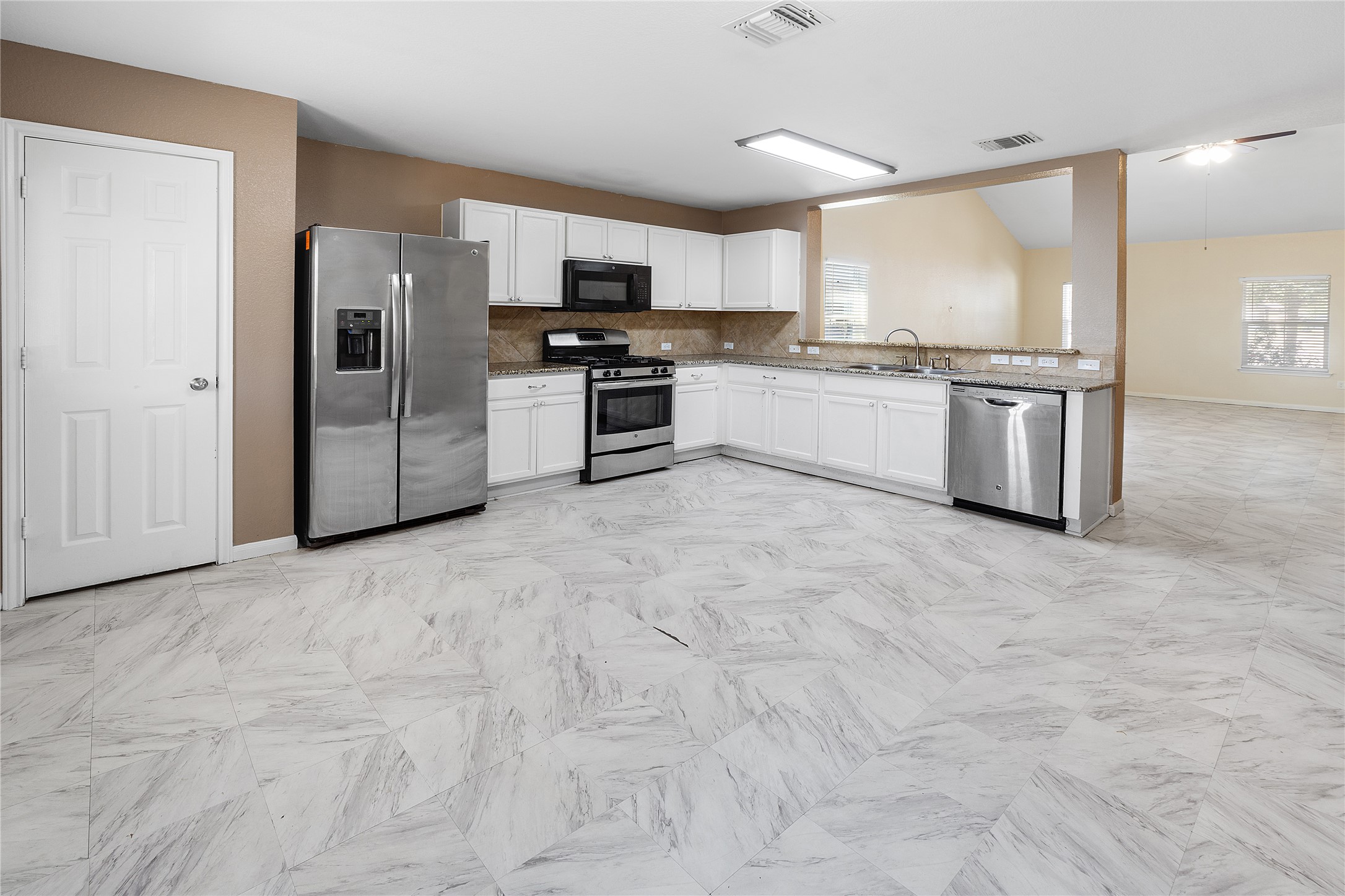 18436 Weatherby Lane Elgin, TX 78621 - Photo 6 of 23 Kitchen featuring appliances with stainless steel finishes, tasteful backsplash, white cabinetry, and healthy amount of natural light