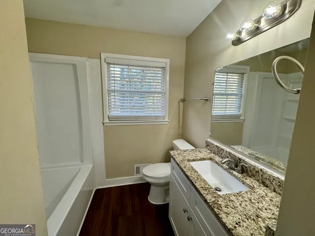 a bathroom with a granite countertop sink a toilet a mirror a vanity and shower