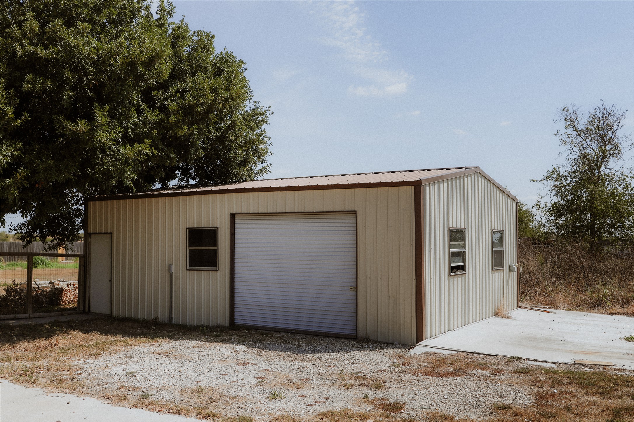 17323 Manda Carlson Road Manor, TX 78653 - Photo 28 of 29 A detached metal workshop sits on a gravel lot under clear skies.