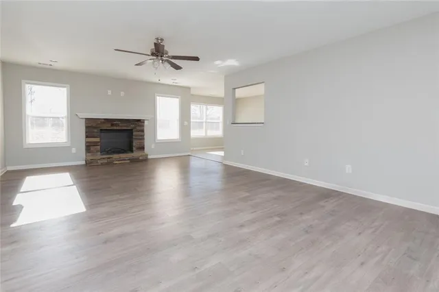 an empty room with wooden floor fireplace and windows