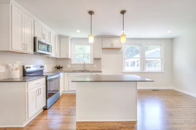 a kitchen with stainless steel appliances granite countertop a sink a window and white cabinets