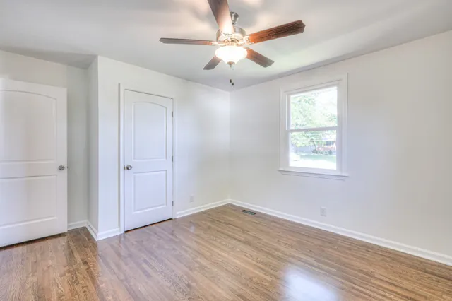 an empty room with wooden floor ceiling fan and windows