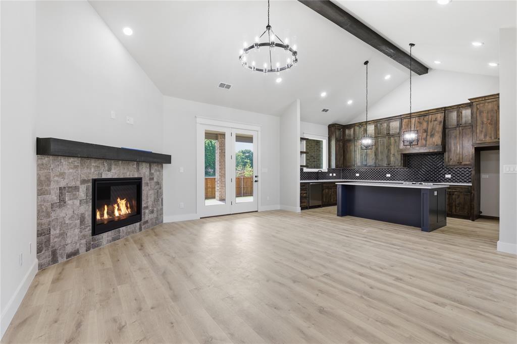 713 Anne Road Van Alstyne, TX 75495 - Photo 5 of 29 Open-concept interior featuring light wood-finish flooring, vaulted ceilings, and a corner fireplace with stone tile surround