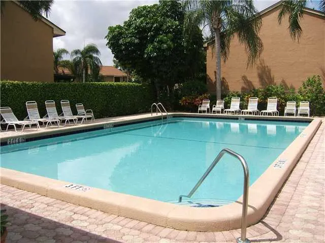 a view of a swimming pool with a lawn chairs under palm trees