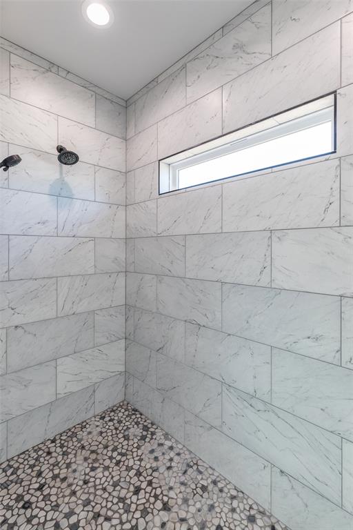 107 Kleingrass Road Abilene, TX 79606 - Photo 17 of 33 Shower enclosure featuring white tile walls with subtle veining, a pebble-stone floor, a recessed horizontal window, and a recessed ceiling light