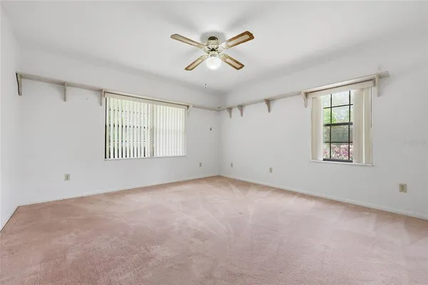 an empty room with ceiling fan and windows
