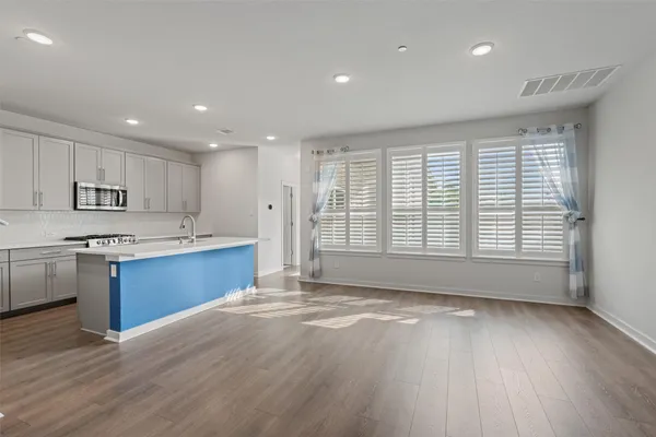 a large kitchen with stainless steel appliances granite countertop a large counter top a wooden floors and a large window