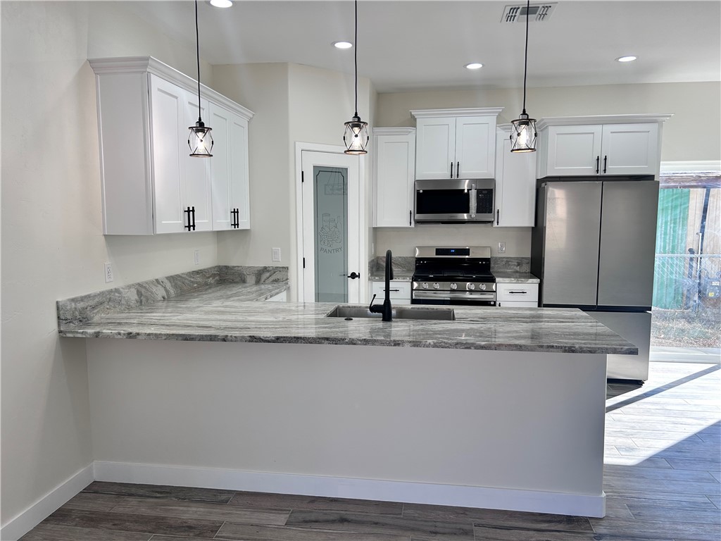 1266 Wilson Road Bullhead City, AZ 86442 - Photo 7 of 29 Kitchen featuring a peninsula, stainless steel appliances, white cabinets, light stone counters, and decorative light fixtures