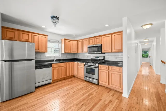 a kitchen with granite countertop wooden floors stainless steel appliances a sink and a window