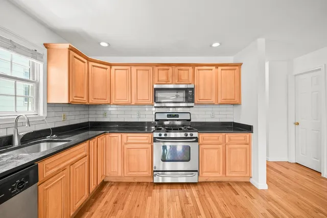 a kitchen with stainless steel appliances granite countertop wooden cabinets a sink and dishwasher a stove with wooden floors