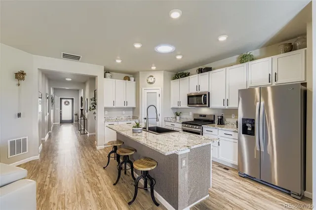 a kitchen with stainless steel appliances a refrigerator a stove a sink dishwasher a oven with white cabinets and wooden floor