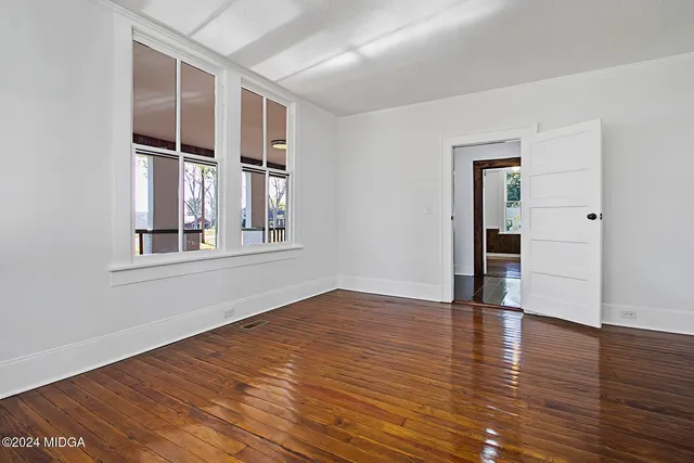 a view of an empty room with wooden floor and windows
