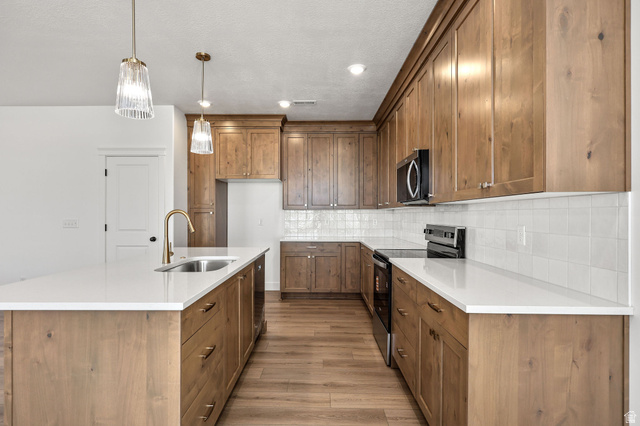 1661 West Ross Road Syracuse, UT 84075 - Photo 9 of 28 Kitchen featuring range with electric cooktop, wood finish cabinetry, an island with sink, pendant lighting, and decorative backsplash