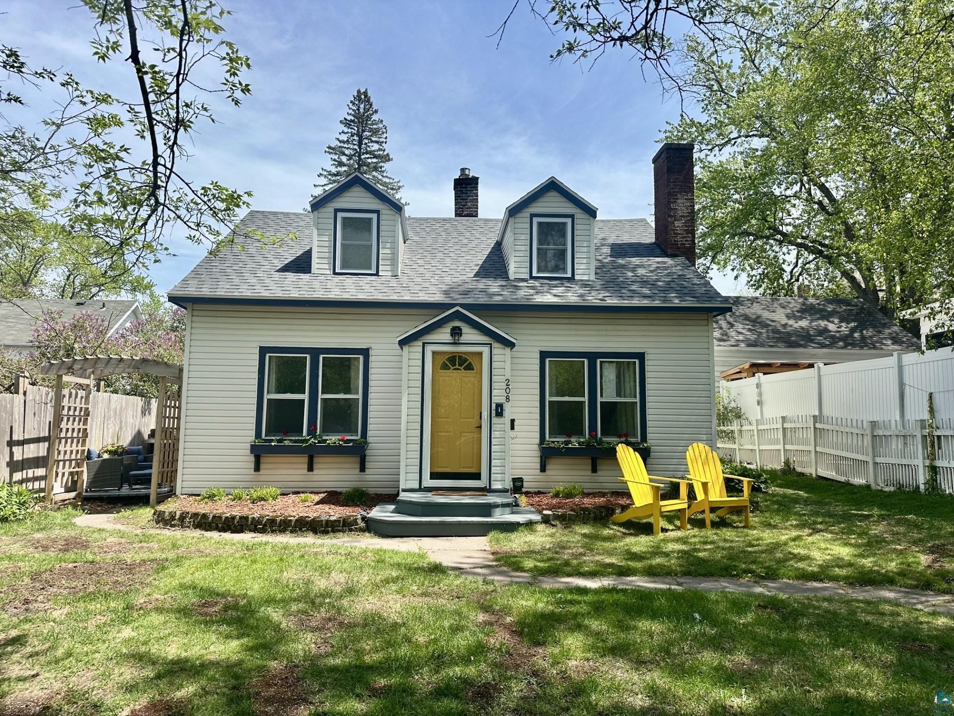208 Chestnut Street Cloquet, MN 55720 - Photo 1 of 24 Charming residence featuring dormer windows, a bright yellow front door with a transom, and dark trim details