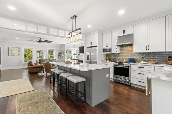 a kitchen with stainless steel appliances kitchen island granite countertop a sink dishwasher a stove a refrigerator and cabinets with wooden floor