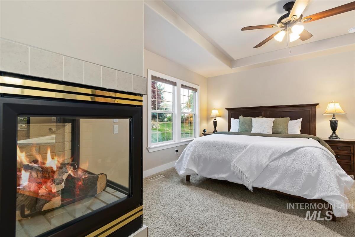 10462 West Lanktree Gulch Road Star, ID 83669 - Photo 19 of 48 Bedroom featuring a tile-surround fireplace with brass accents, tray ceiling, ceiling fan with integrated lighting, window, and carpet flooring