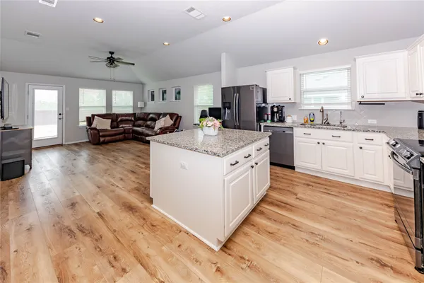 a large white kitchen with kitchen island a stove a sink dishwasher a refrigerator white cabinets with wooden floor