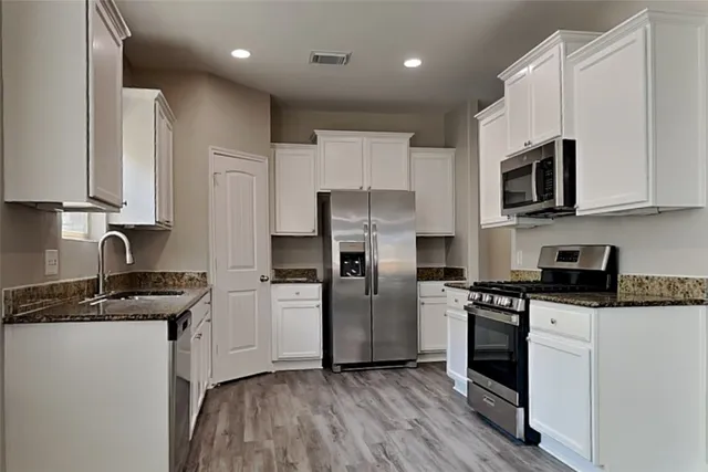 a kitchen with granite countertop a sink a counter top space stainless steel appliances and cabinets
