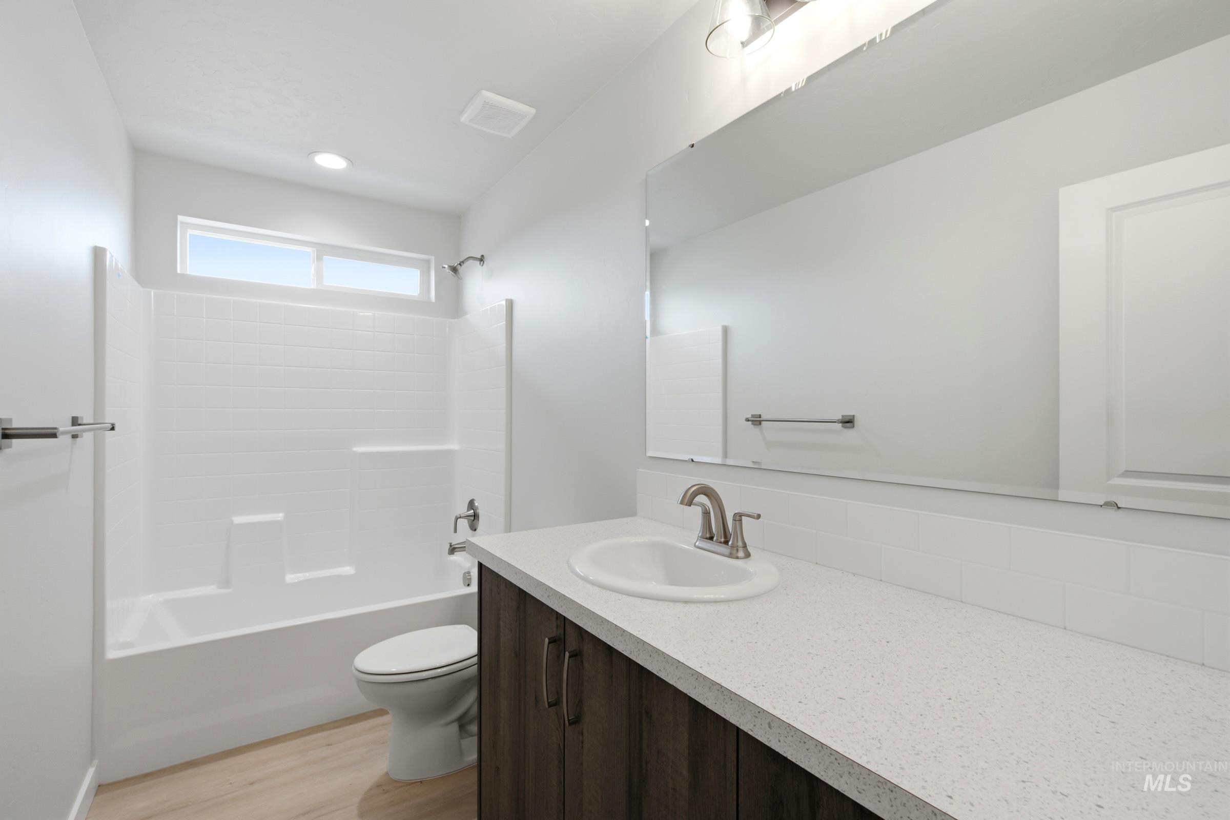 13324 Bank Street Caldwell, ID 83607 - Photo 23 of 29 Bathroom featuring a white subway tile shower surround, a sleek white vanity countertop, a dark wood-finish vanity, and light wood-finish flooring