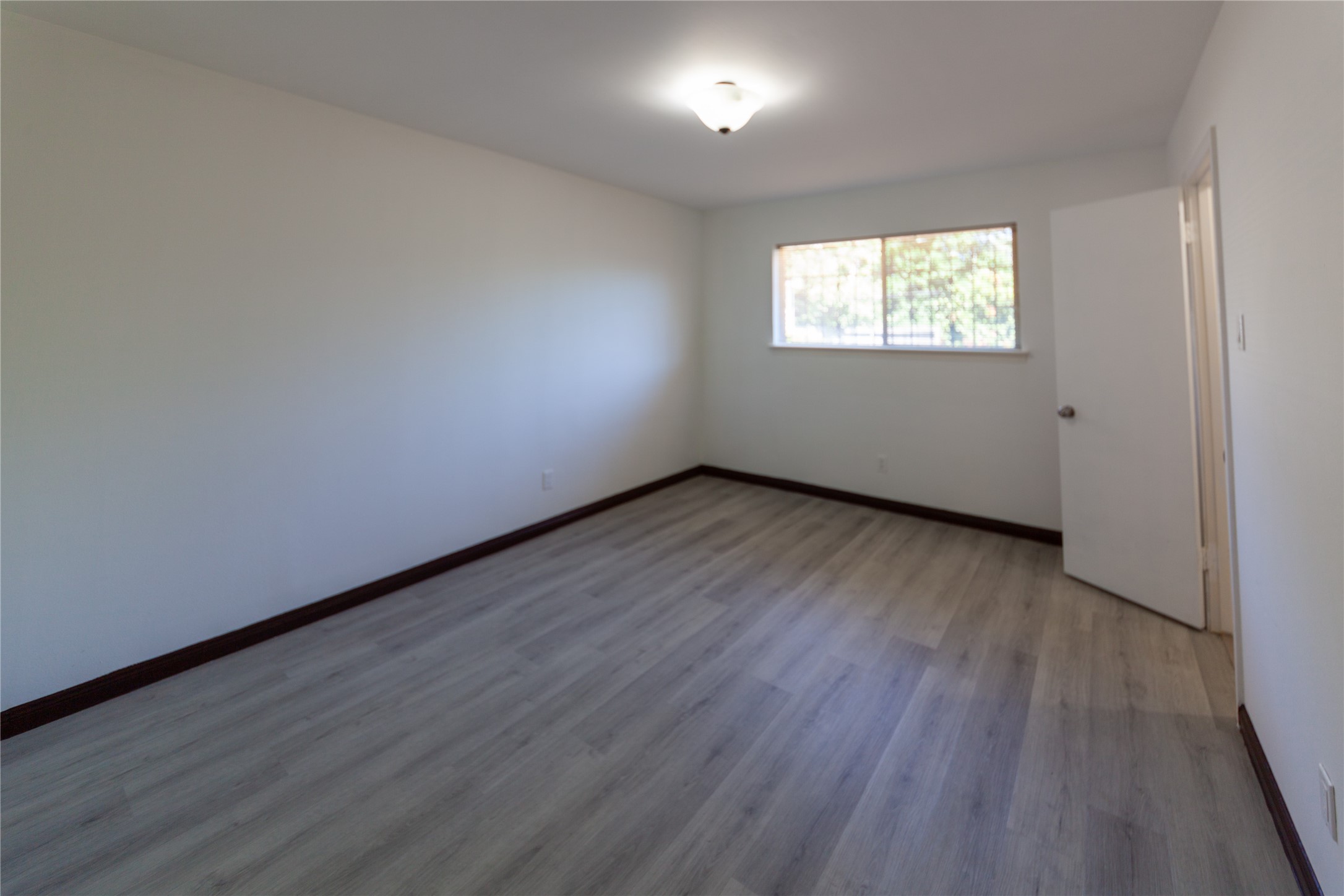 8826 Roos Road Houston, TX 77036 - Photo 31 of 42 Bed room 3 features light laminate flooring, a neutral painted wall, and a window allowing natural light. It includes a simple ceiling light fixture and an open door, offering a clean, spacious feel.