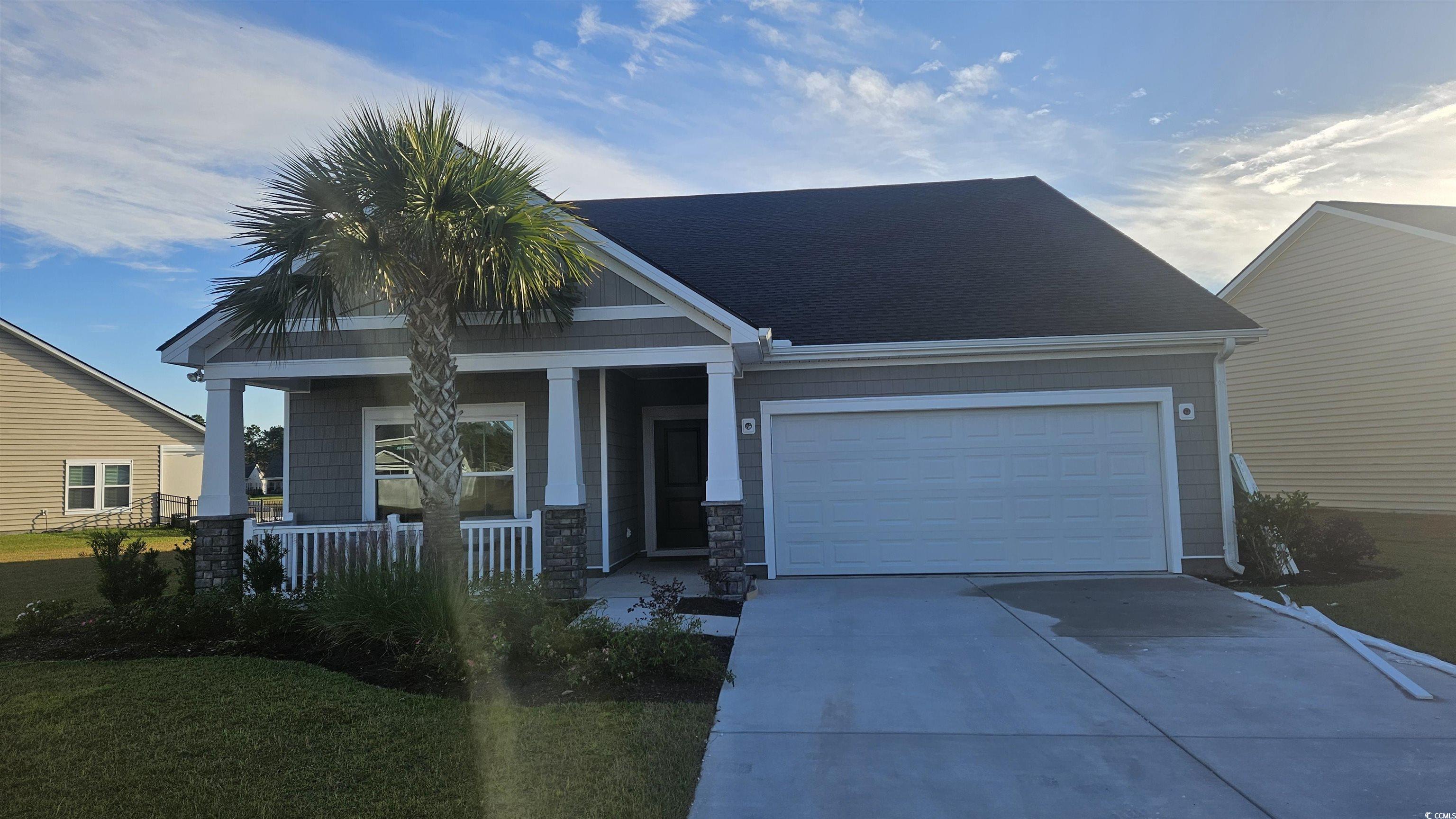 View of front of house featuring covered porch, driveway, a garage, roof with shingles, and a front lawn