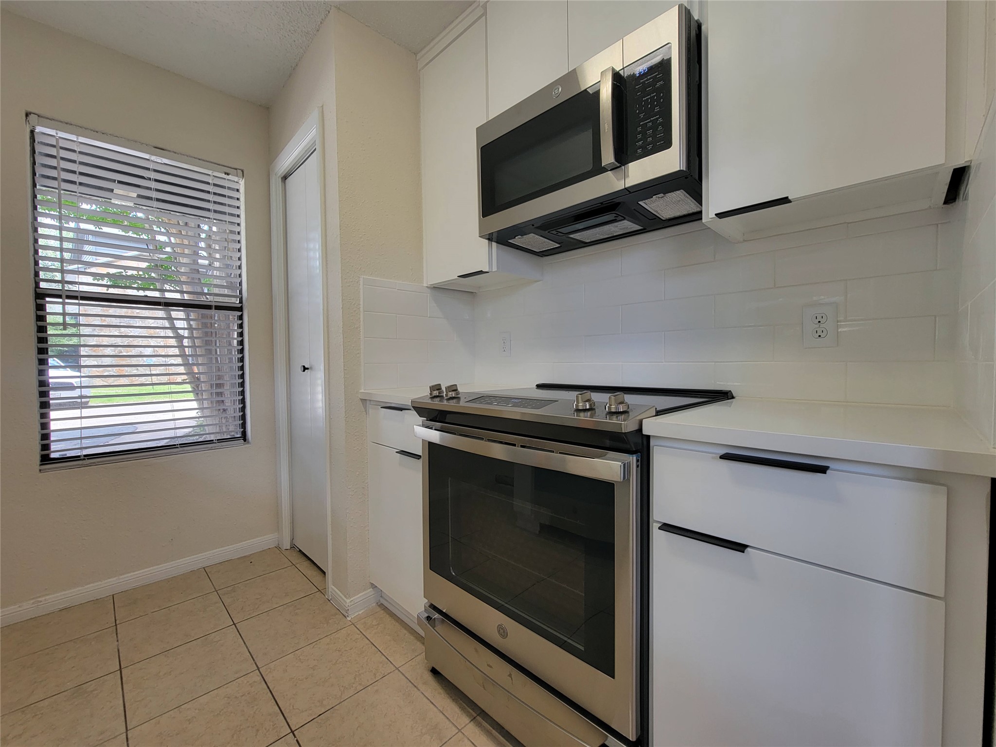 8706 Schick Road, Unit A Austin, TX 78729 - Photo 10 of 33 A well-lit kitchen featuring contemporary white cabinetry, stainless steel appliances, and durable tile flooring.