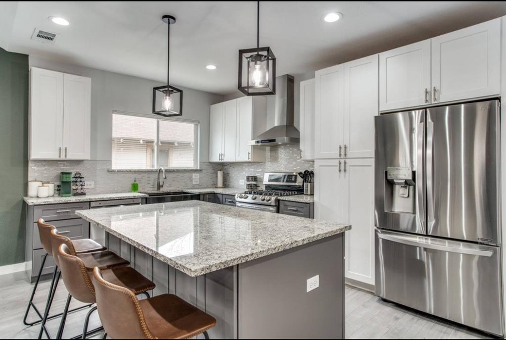 1606 West 12th Street Dallas, TX 75208 - Photo 6 of 20 Kitchen featuring appliances with stainless steel finishes, gray cabinets, wall chimney range hood, decorative light fixtures, and tasteful backsplash