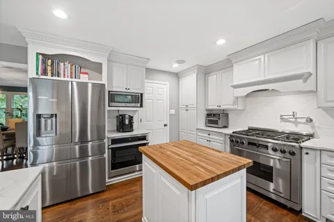 a kitchen with stainless steel appliances kitchen island granite countertop a refrigerator a stove a sink dishwasher and white cabinets with wooden floor