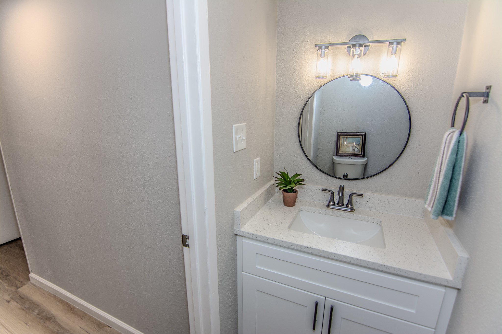 13009 Wirevine Lane Houston, TX 77072 - Photo 11 of 18 Half bathroom features a modern vanity with a sleek white countertop and under-mount sink. A round mirror and stylish light fixture enhance the space.