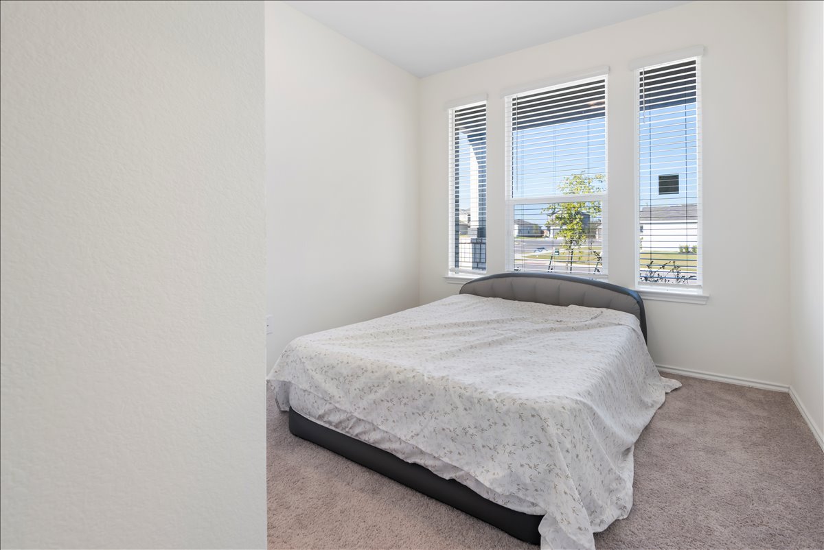 18501 Spotted Eagle Lane Elgin, TX 78621 - Photo 15 of 40 Natural light floods this inviting bedroom, featuring soft carpeting and tall windows.