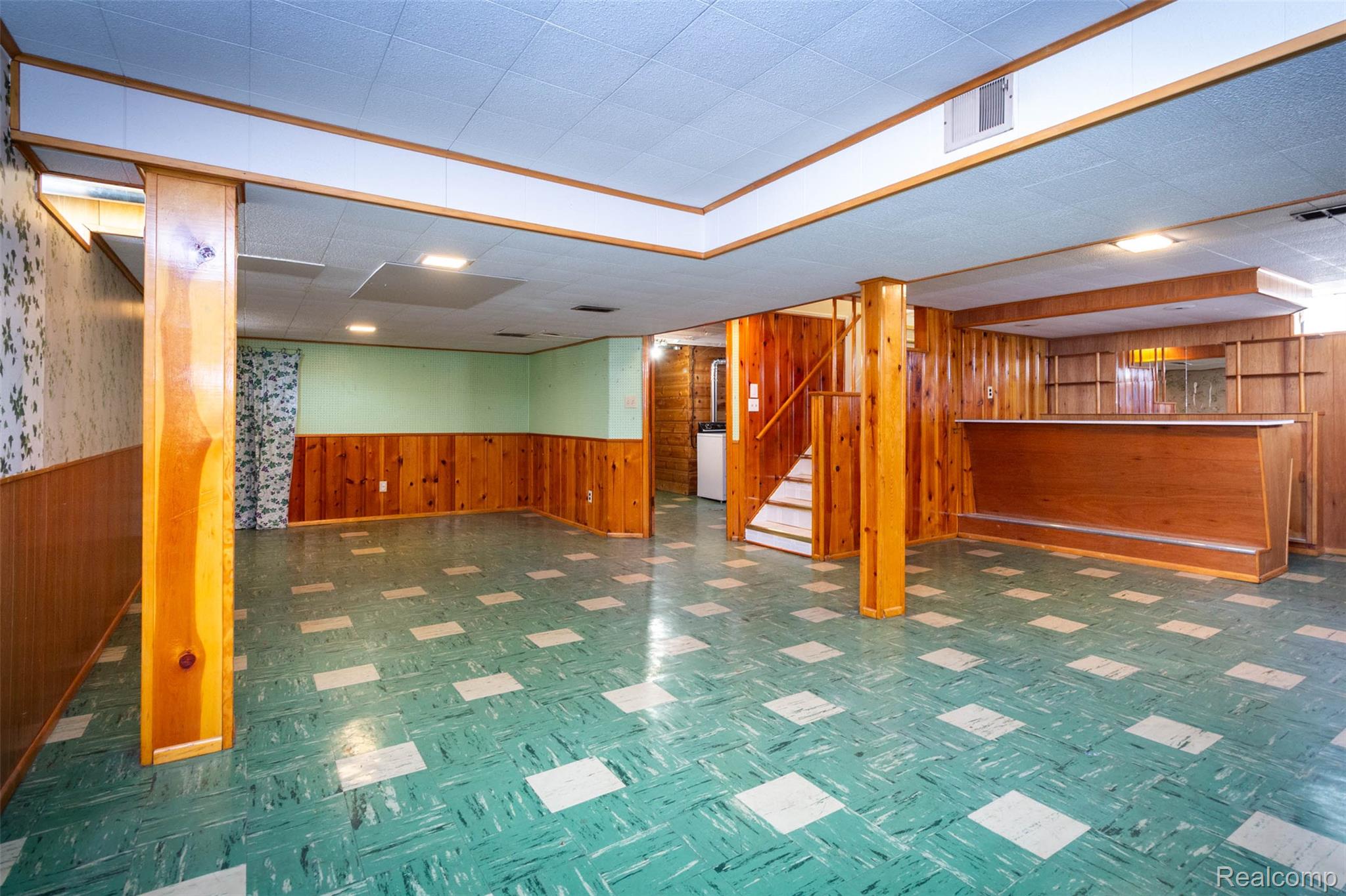 14869 Champaign Road Allen Park, MI 48101 - Photo 24 of 34 Spacious lower level featuring wood paneling, a built-in bar, wood-finish columns, a staircase with wood-finish railing, and patterned flooring
