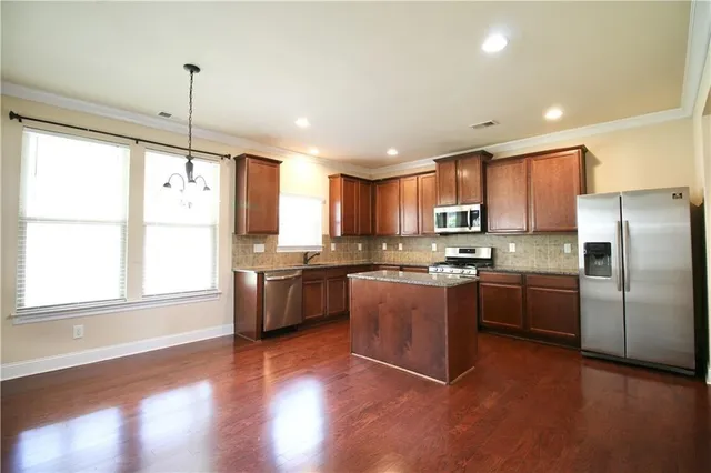 a kitchen with stainless steel appliances granite countertop a refrigerator a sink dishwasher a stove and white countertops with wooden floor