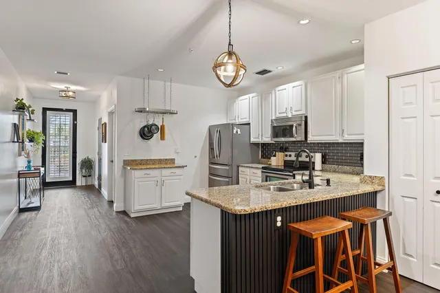 a kitchen with stainless steel appliances granite countertop a sink a stove a refrigerator cabinets and chairs